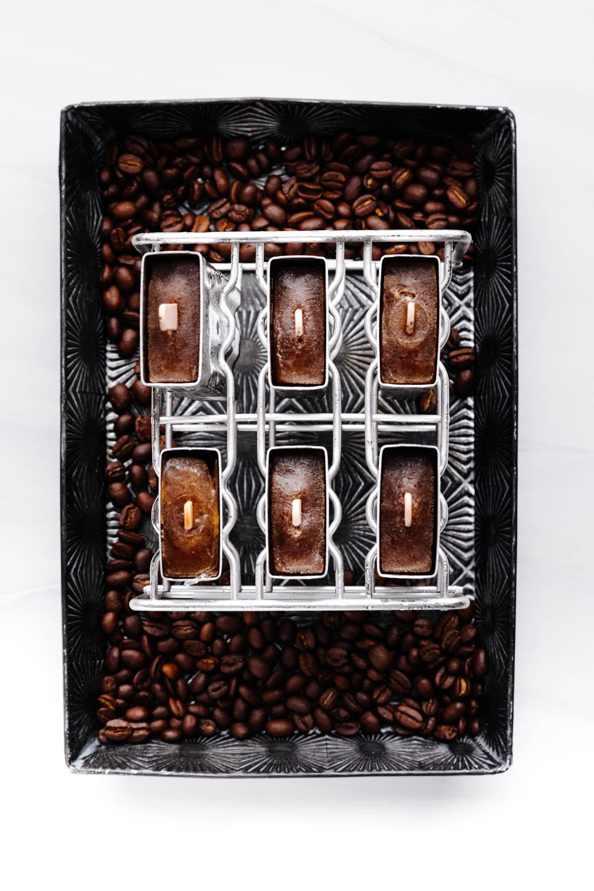 Frozen stainless steel popsicle molds with wooden popsicle sticks in it on a backdrop of coffee beans