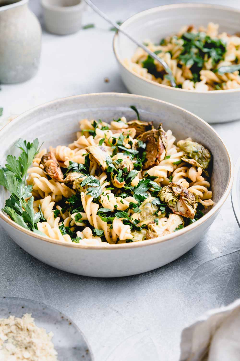 Brussels sprout pasta in a round bowl on a light backdrop with a pasta bowl in the back and small bowls