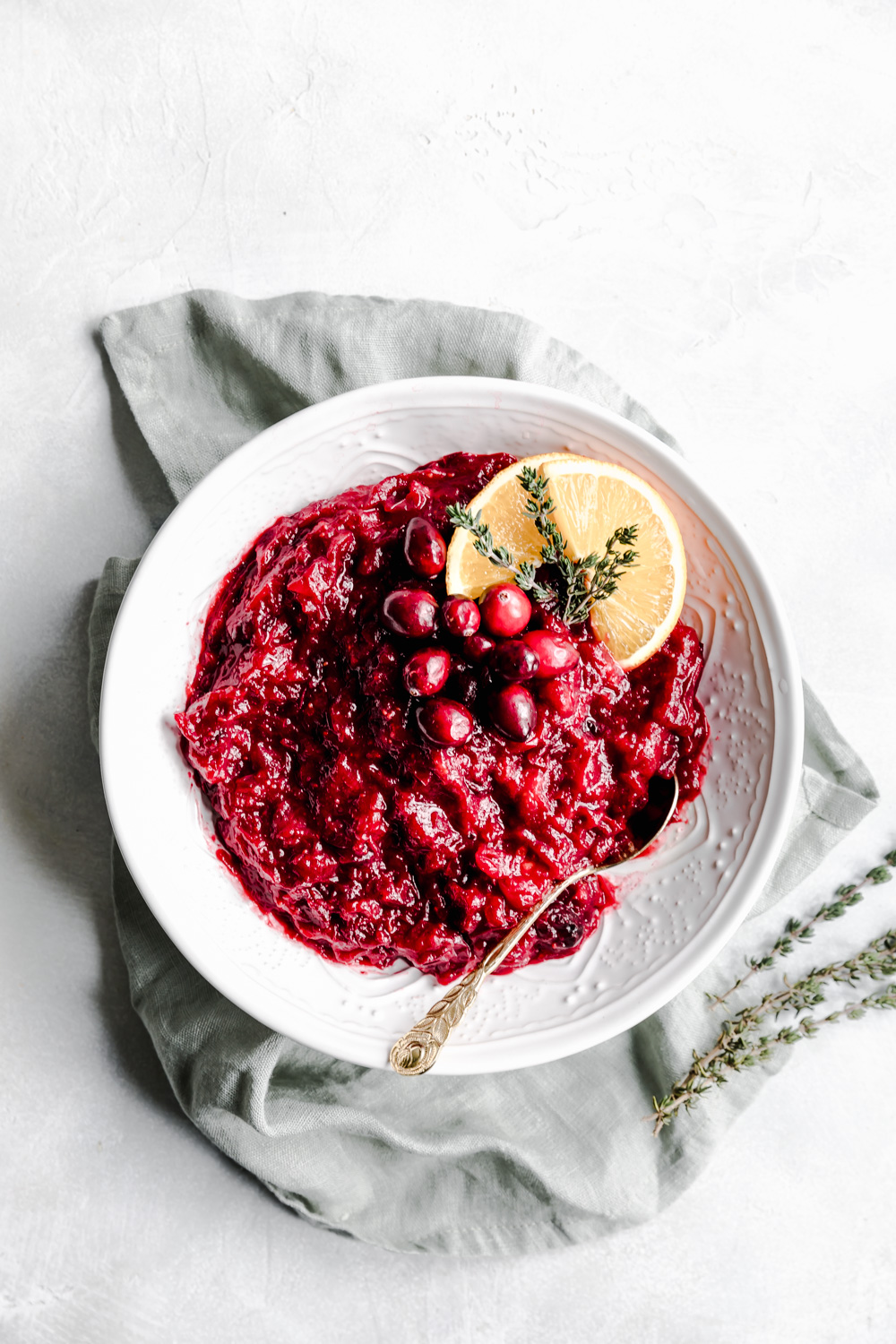 cranberry sauce in white bowl decorated with orange slices, cranberries and thyme