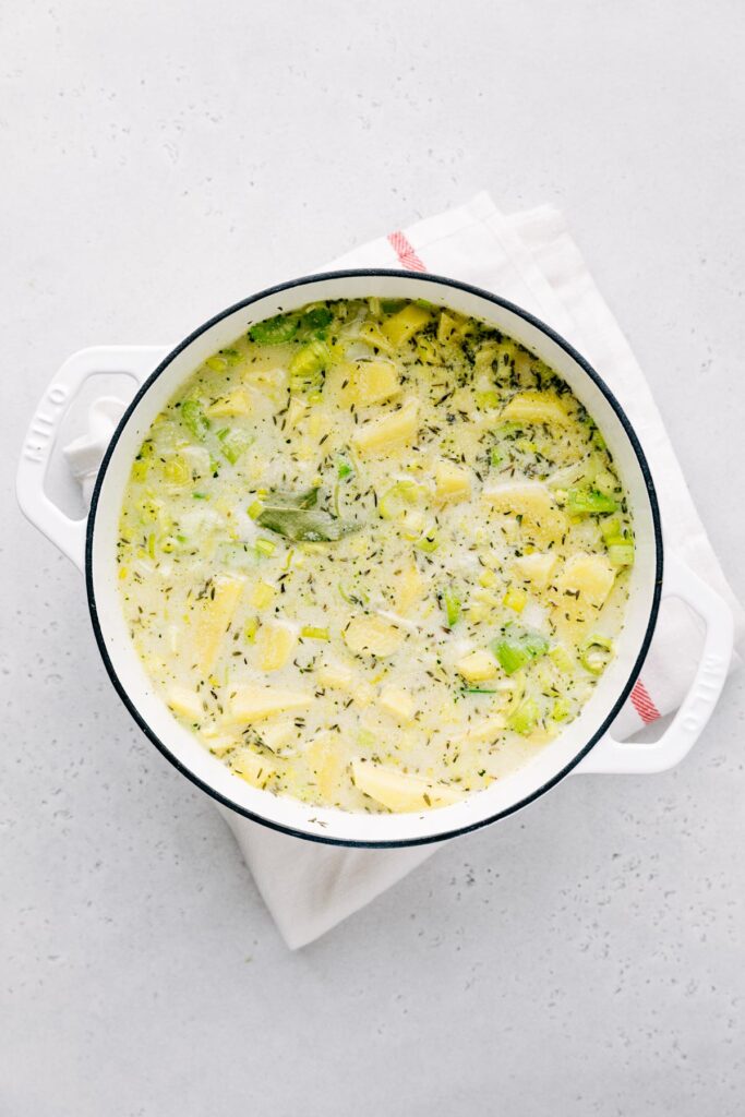 Potato leek soup in a white pot on a light backdrop with a white napkin underneath