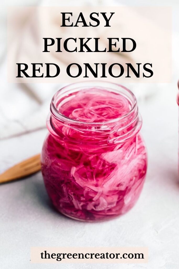 A glass jar with pickled red onions on a light grey backdrop with a white napkin and a wooden fork in the back