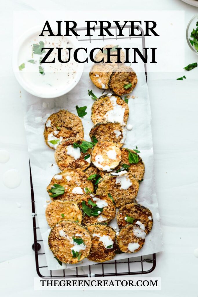 Air fryer zucchini slices on a cooling rack on white paper topped with herbs and drizzled with a sauce with the name of the recipe on top