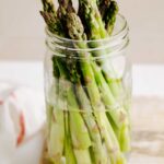A mason jar filled with water with trimmed asparagus in it.