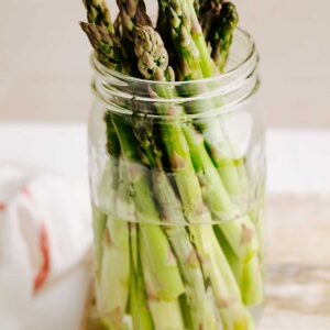 A mason jar filled with water with trimmed asparagus in it.