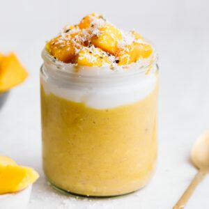 Mango Overnight Oats in a glass pot topped with coconut yogurt and fresh mango with coconut flakes.