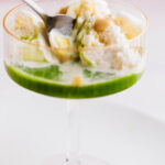 Glass of matcha affogato with vanilla ice cream, green matcha tea, and caramel sauce, served with a spoon.