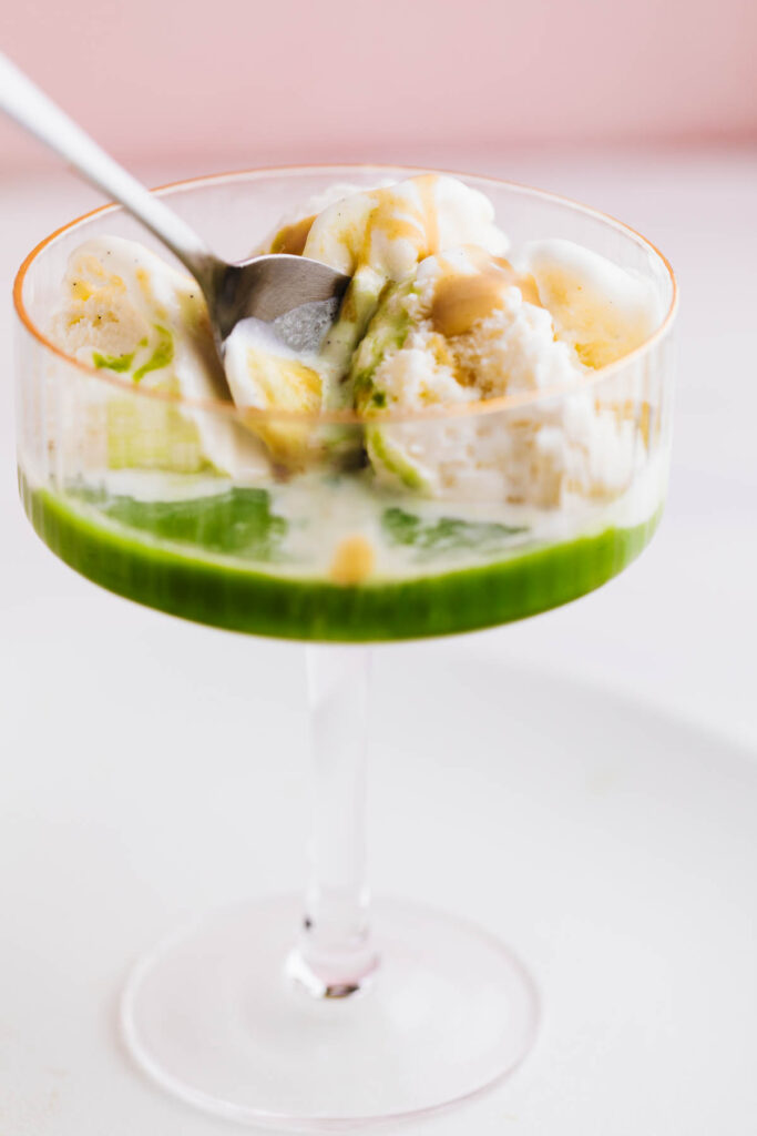 Glass of matcha affogato with vanilla ice cream, green matcha tea, and caramel sauce, served with a spoon.