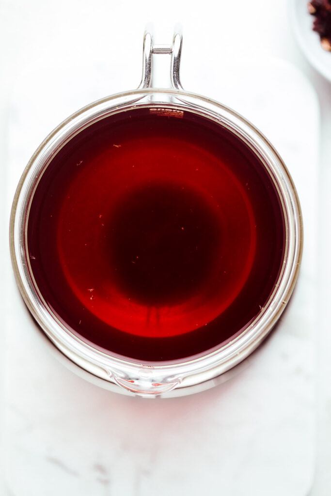 A glass teapot with dark red tea in it viewed from the top.