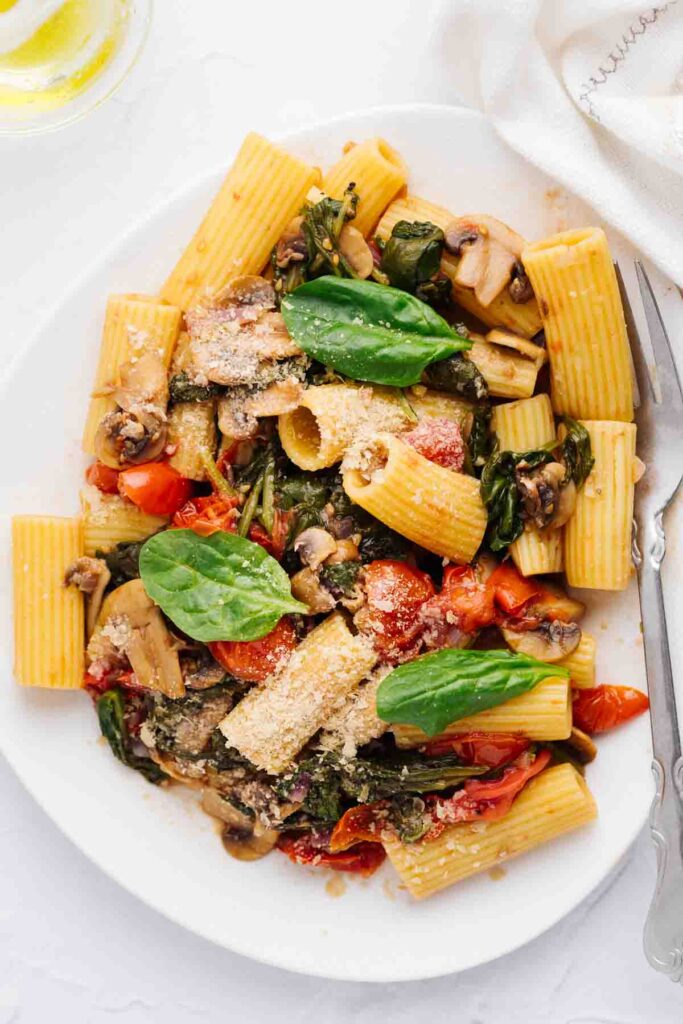 Pasta fresca topped with nutritional yeast and spinach leaves on a white plate with a silver fork.