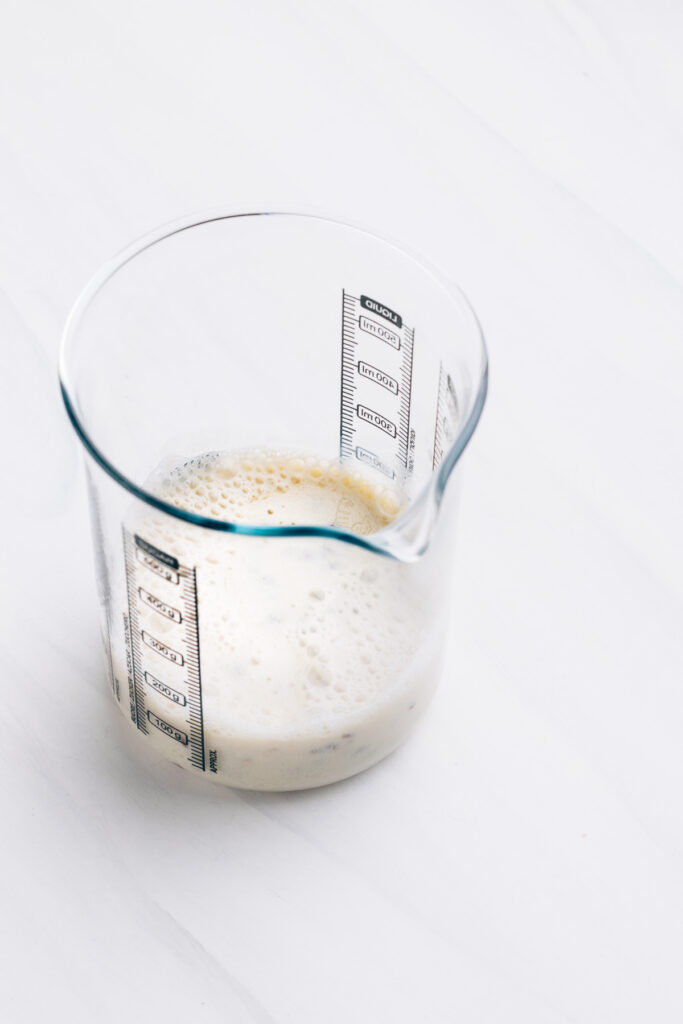 A measuring glass with almond milk on a white backdrop