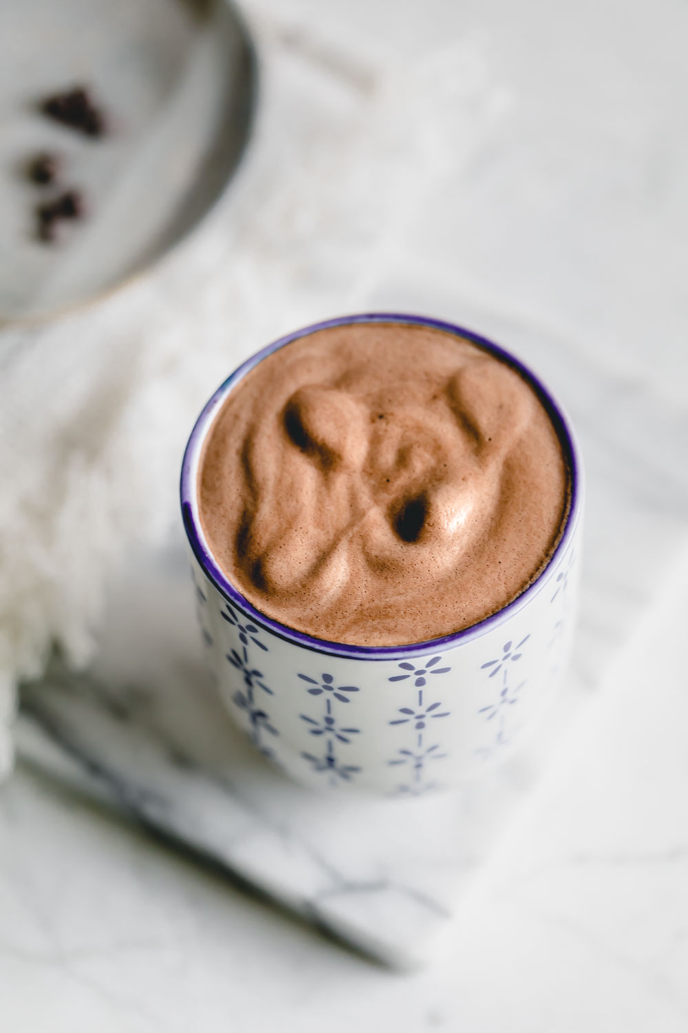 Vegan hot chocolate drink in a blue and white mug on a white backdrop with a marble board