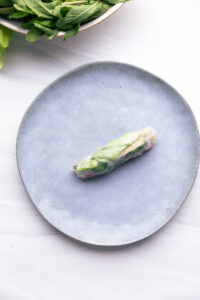 A blue plate with a summer rolls in the middle with the filling visible