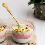 Christmas smoothie in small glass topped with chopped pistachio nuts with a gold teaspoon on a wooden cutting board