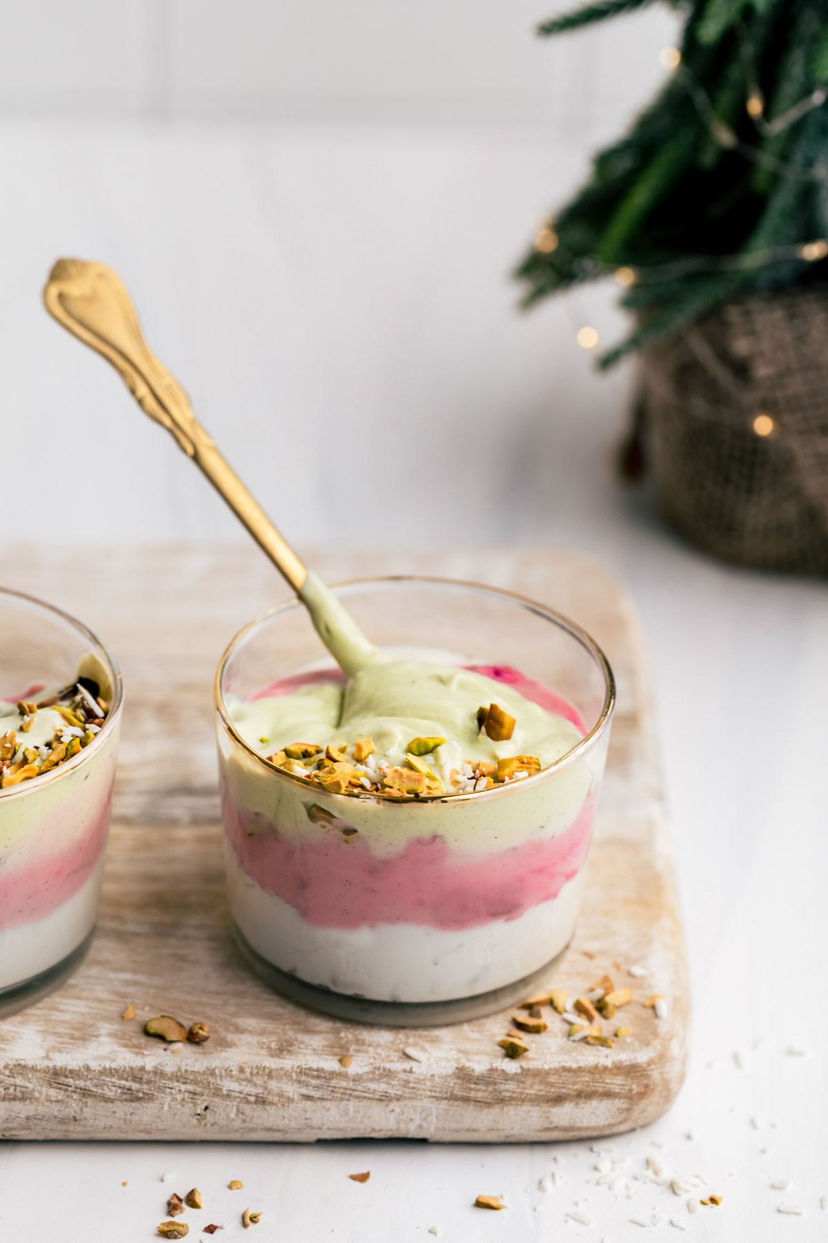 Christmas smoothie in small glass topped with chopped pistachio nuts with a gold teaspoon on a wooden cutting board