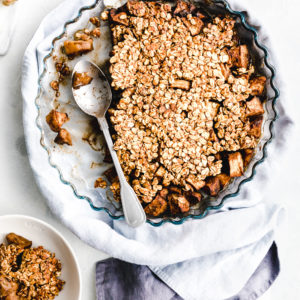 Vegan Apple Crisp in the mold with a spoon on a white backdrop with a blue napkin